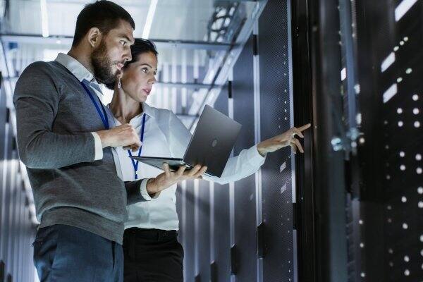 A man holding a laptop standing next to a woman pointing at a control panel