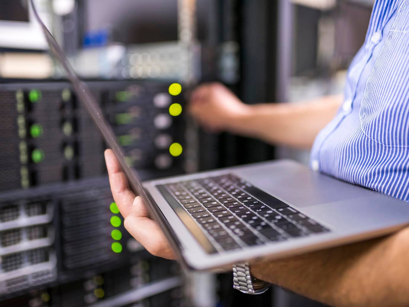 Man working on laptop and maintaining servers in data center